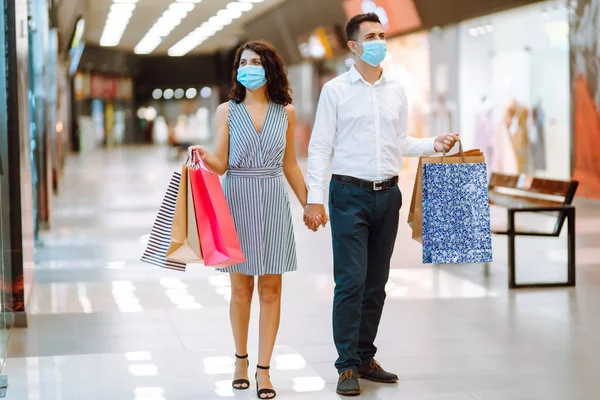 ショッピングバッグがモールを歩いて保護医療用マスクで若い愛情のカップル コロナウイルスの流行中の買い物 消費主義 ブラックフライデーの概念 — ストック写真