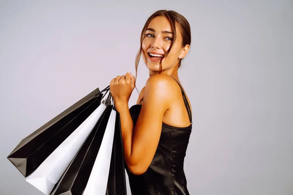 一个漂亮的 情绪化的年轻女子的画像 她通过灰色的墙背景 拿着购物袋 显得孤立无援 购物后穿着黑色衣服的优雅女人 黑色星期五 消费主义 生活方式 — 图库照片