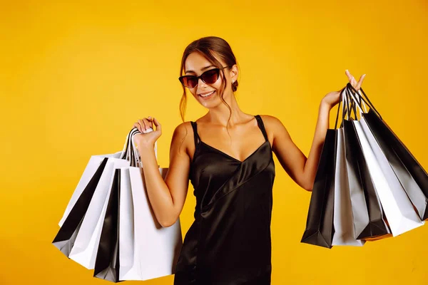 时尚女人喜欢购物 身穿黑色女装 戴着墨镜 背景呈黄色的优雅女人 消费主义 黑色星期五概念 — 图库照片
