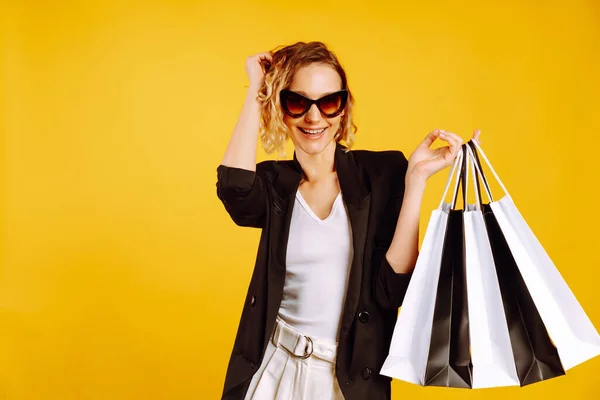 漂亮的女人在黄色的背景下摆姿势购物后 一个拿着黑白购物袋的年轻女人采购 黑色星期五 销售概念 — 图库照片