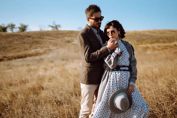 Stylish  young couple enjoying autumn weather in autumn field. Lovely couple walking and hugging in the field together. The concept of youth, love and lifestyle.