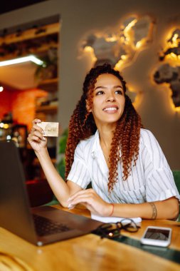 Kredi kartı ve dizüstü bilgisayarı olan Afrikalı Amerikalı bir kadın kafe veya restoranda online alışveriş yapıyor. Çevrimiçi alışveriş, e-ticaret, internet bankacılığı, harcama.