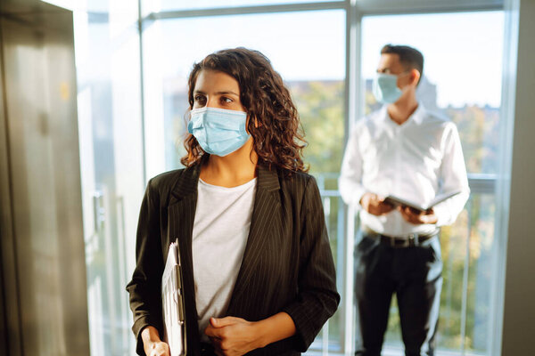 Портрет деловой женщины в защитной маске во время вирусной эпидемии, стоящей возле лифта в современном офисе. Офис-менеджер вернулся к работе в офисе после карантина. Ковид-19.