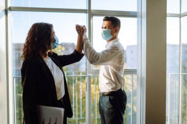Two colleagues in protective sterile mask bumping elbows while greeting each other at work in modern office. Business partners back at work in office after quarantine. Covid-19. clipart