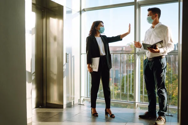 Business woman in protective sterile mask hand showing a stop sign. Stop COVID-19. Business partners back at work in office after quarantine. Meeting near elevator.