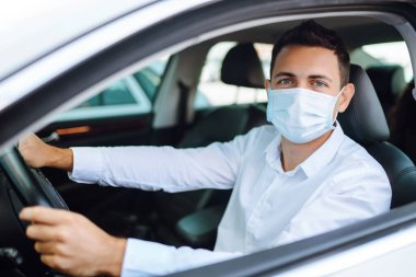 Koruyucu tıbbi maskeli genç adam araba kullanıyor. Koronavirüs salgını sırasında güvenlik, salgın covid-19. İzolasyonu taşı.