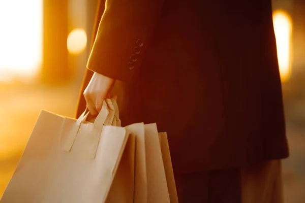Hand of young man with paper bags with purchases at sunset. Young man after autumn shopping. Consumerism, shopping, black friday, sales, lifestyle concept.