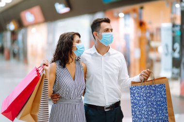 Güzel bir çift alışveriş merkezinde koruyucu tıbbi maske alışverişinde. Alışveriş torbaları tutan mutlu bir çift, alışveriş merkezinde dururken gösteriye bakıp gülümsüyorlar. Covid 2019.