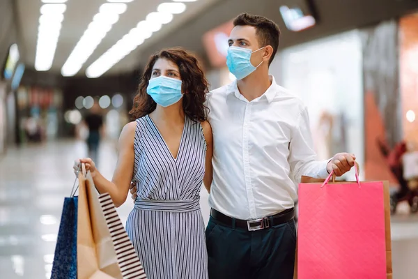 モール内の保護医療用マスクショッピングで美しいカップル ショッピングバッグを持って幸せなカップルは ショーケースを見て モールに立って笑顔 Covid 2019 — ストック写真