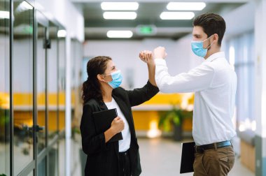 Modern ofiste birbirini selamlarken, koruyucu tıbbi maskeli iki yönetici dirseklerini birbirine vuruyor. Coronavirus sırasında iş ortakları el sıkışır. Covid 19.