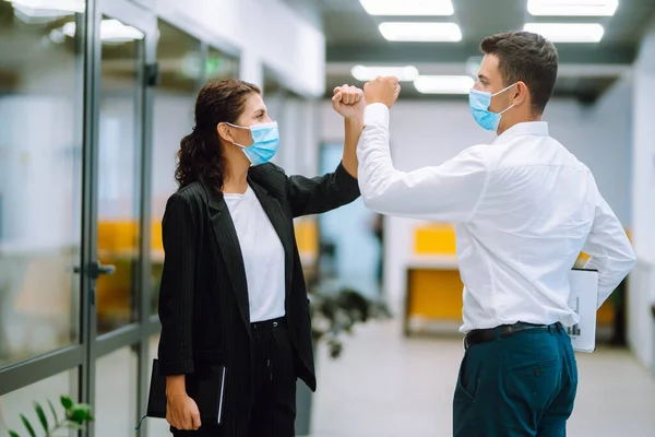 Modern ofiste birbirini selamlarken, koruyucu tıbbi maskeli iki yönetici dirseklerini birbirine vuruyor. Coronavirus sırasında iş ortakları el sıkışır. Covid 19.