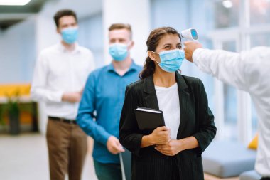 Vücut sıcaklığı kontrolü. Koruyucu yüz maskeleri takan ofis çalışanları girişte sıcaklık taramasından geçiriliyor. Salgın virüs salgını konsepti. COVID-19.