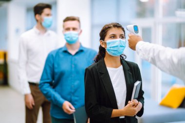 Vücut sıcaklığı kontrolü. Koruyucu yüz maskeleri takan ofis çalışanları girişte sıcaklık taramasından geçiriliyor. Salgın virüs salgını konsepti. COVID-19.