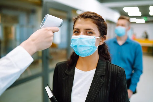 Body Temperature Control. Office staff  in protective face masks undergo temperature screening at the entrance. Epidemic virus outbreak concept. COVID-19.