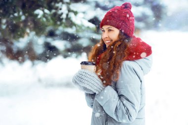  Sıcak bir fincan kahveyle birlikte kışın giydiği güler yüzlü kadın. Parkta ya da ormanda kış yürüyüşü. İnsanlar, sezon, içkiler, tatil ve Noel konsepti.         