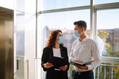 Koruyucu maskeli iki iş arkadaşı projeyi tartışıyor, fikirleri paylaşıyor, asansörün yanında hoş sohbetler ediyorlar. Karantina sırasında ofiste çalış. Covid 19.