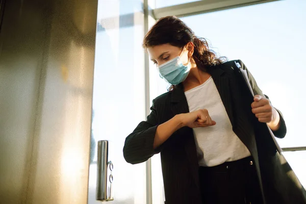 保護滅菌マスクのビジネス女性は 現代のオフィスで手を使用しないようにエレベーターボタンを押すために肘を使用します Covid — ストック写真