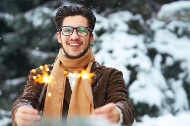 Genç bir adamın ellerinde maytaplar. Palto, süveter, atkı ve gözlüklü şık bir adam kış tatilini kutluyor. Noel, yeni yıl. Kış yaşam tarzı.