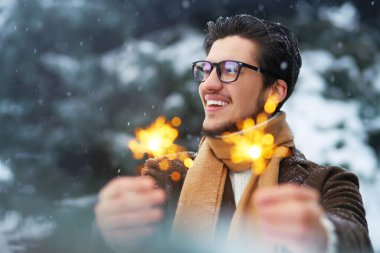 Genç bir adamın ellerinde maytaplar. Palto, süveter, atkı ve gözlüklü şık bir adam kış tatilini kutluyor. Noel, yeni yıl. Kış yaşam tarzı.