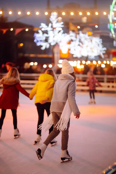 夕方のクリスマスの祭典のリンクで若い女性のアイススケート 冬のスタイルの服のスケートで笑顔の女性 冬休みのコンセプト 周囲の光 — ストック写真