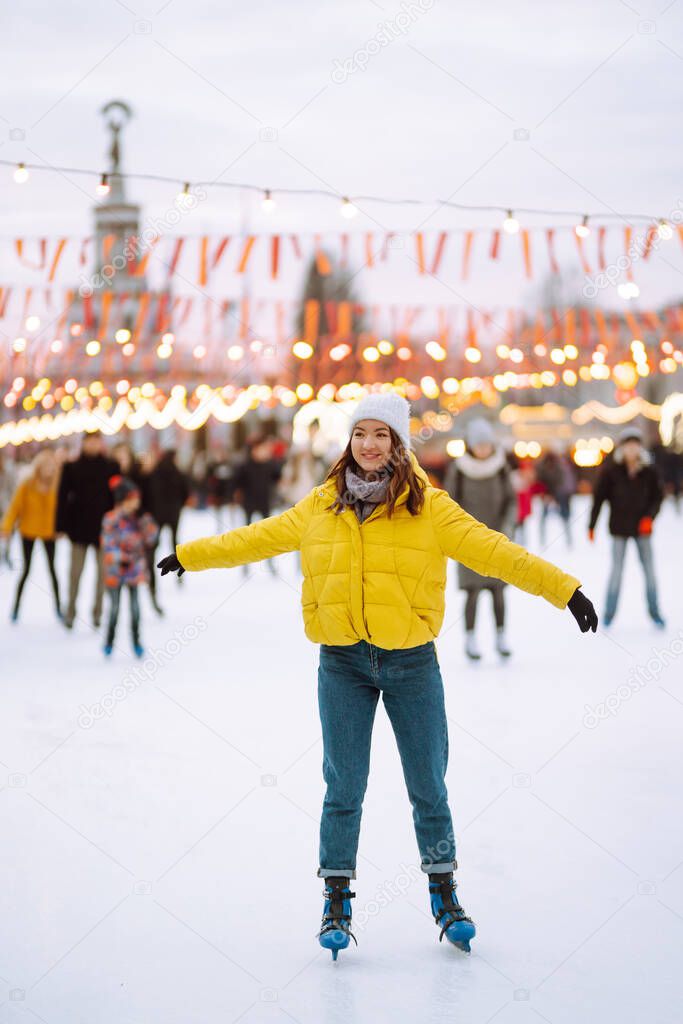 Beautiful woman have fun, active ice skating on the ice arena in the city square in winter on Christmas Eve. Winter holidays concept. Lights around.