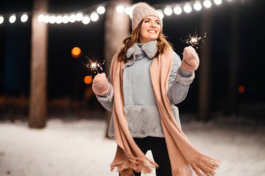 Noel 'in ışıltısı ellerde. Kış ormanında parıltı tutan neşeli genç bir kadın. Şenlikli çelenk ışıkları. Noel, yeni yıl.