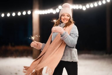 Noel 'in ışıltısı ellerde. Kış ormanında parıltı tutan neşeli genç bir kadın. Şenlikli çelenk ışıkları. Noel, yeni yıl.