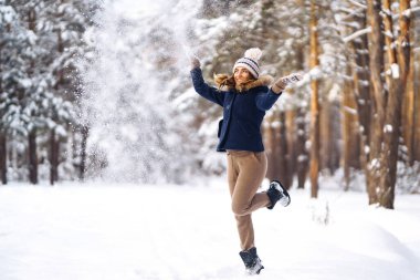 Kış tatilin kutlu olsun. Karlı ormanda karla oynayan tatlı bir kadın. Kışlık elbiseli genç bayan kışın tadını çıkarıyor. Kış tatili.
