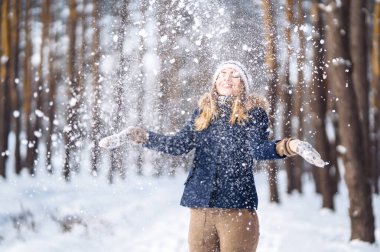 Kış tatilin kutlu olsun. Karlı ormanda karla oynayan tatlı bir kadın. Kışlık elbiseli genç bayan kışın tadını çıkarıyor. Kış tatili.