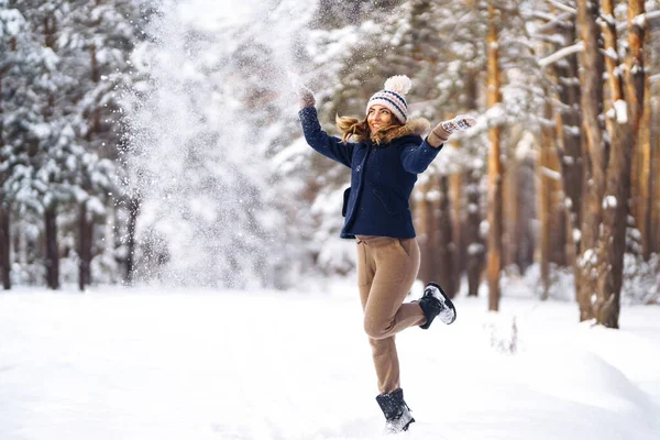 Kış tatilin kutlu olsun. Karlı ormanda karla oynayan tatlı bir kadın. Kışlık elbiseli genç bayan kışın tadını çıkarıyor. Kış tatili.