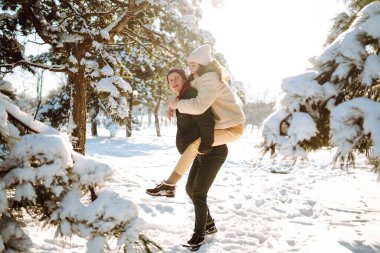 Mutlu çift kar ormanlarında yürüyüp eğleniyor. Genç adam ve kadın kış tatillerinde karda oynuyorlar. Noel, yeni yıl. Kış yaşam tarzı.