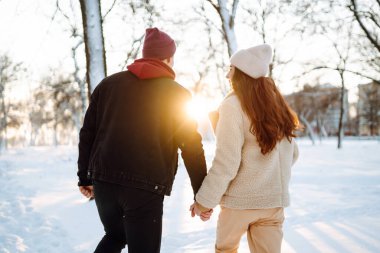 Genç çift kışın gün batımında dışarıda sarılıp gülüyor. Mutlu adam ve kadın kar ormanlarında eğleniyorlar. Tatiller, mevsimler, aşk ve eğlence kavramı.
