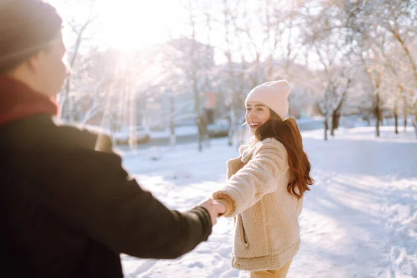 Happy couple hugging and kissing outdoors in winter park. Young man and woman enjoy each other in snow forest. Holidays, season, love and leisure concept.