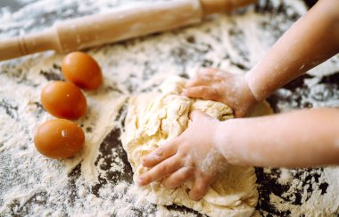 Çocuklar hamur yoğurmak için hamur yoğurdu. Çocuk elleri, biraz un, buğday hamuru ve siyah masanın üzerinde merdane. Noel için kurabiyeler.