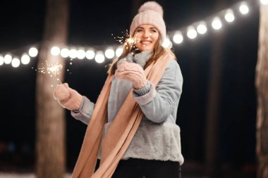 Kış ormanında parıltı tutan neşeli genç bir kadın. Şenlikli çelenk ışıkları. Noel, yeni yıl.