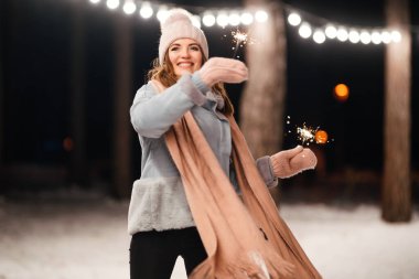 Kış ormanında parıltı tutan neşeli genç bir kadın. Şenlikli çelenk ışıkları. Noel, yeni yıl.