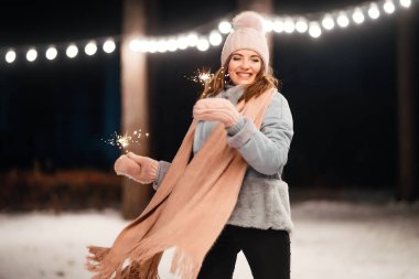 Kış ormanında parıltı tutan neşeli genç bir kadın. Şenlikli çelenk ışıkları. Noel, yeni yıl.