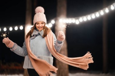 Kış ormanında parıltı tutan neşeli genç bir kadın. Şenlikli çelenk ışıkları. Noel, yeni yıl.