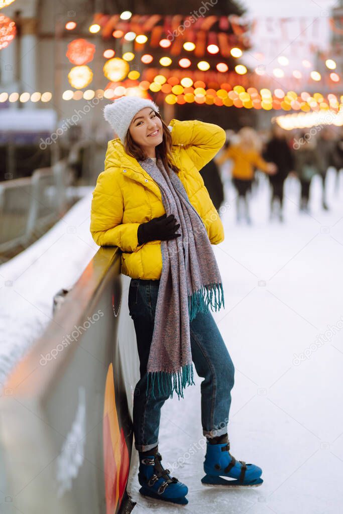 Young  woman ice skating on the ice arena in the city square in winter on Christmas Eve. Happy woman on Christmas market. Holidays, season and active concept.