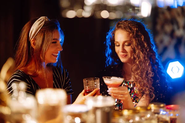 Cheerful women drinking cocktails in bar. Women friends make a toast as they celebrate at a party. Party, celebration, friends, bachelorette party, birthday, winter holidays concept.