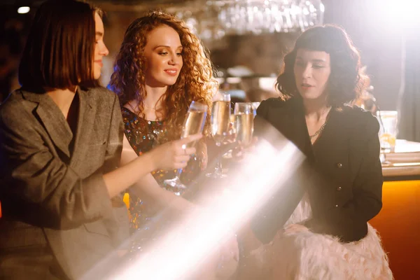 Three Woman with glasses of champagne  at a party. Women friends make a toast elebrating winter holidays together in bar. Friends, bachelorette party, birthday, winter holidays concept.