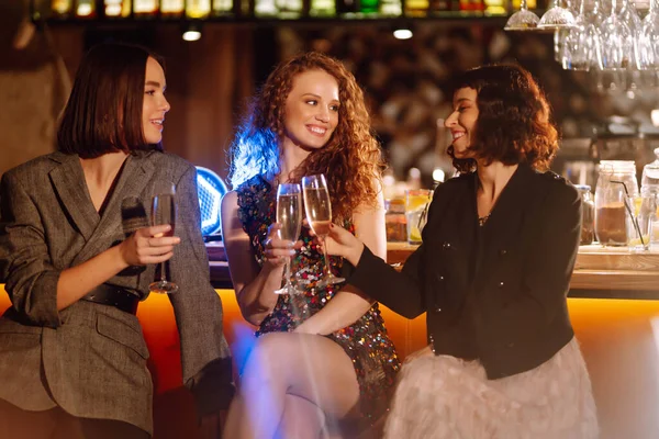 Three Woman with glasses of champagne  at a party. Women friends make a toast elebrating winter holidays together in bar. Friends, bachelorette party, birthday, winter holidays concept.
