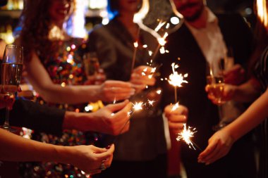 Elinde maytaplar var. Bir grup mutlu insan partide maytap tutuyor. Genç arkadaşlar bir gece kulübünde şampanya bardaklarını tokuşturuyorlar. Kutlama, insanlar ve tatil kavramı.