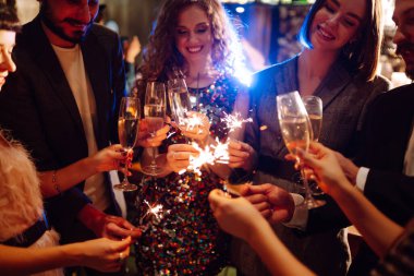 Elinde maytaplar var. Bir grup mutlu insan partide maytap tutuyor. Genç arkadaşlar bir gece kulübünde şampanya bardaklarını tokuşturuyorlar. Kutlama, insanlar ve tatil kavramı.