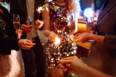 Elinde maytaplar var. Bir grup mutlu insan partide maytap tutuyor. Genç arkadaşlar bir gece kulübünde şampanya bardaklarını tokuşturuyorlar. Kutlama, insanlar ve tatil kavramı.