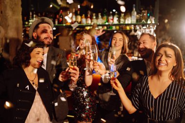 Mutlu arkadaşlar eğlenirken konfeti atıp zıplıyorlar. Bir grup genç, kış tatilini birlikte kutluyor. Konfeti eğlencelidir. Parti, kutlama, içki, doğum günü konsepti.