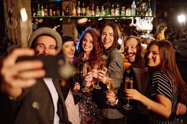 クラブでパーティーを楽しみながら 携帯電話での自撮りを楽しんでいる友人のグループ バーで一緒に冬の休日を祝うシャンパンのグラスを持つ若者のグループ — ストック写真