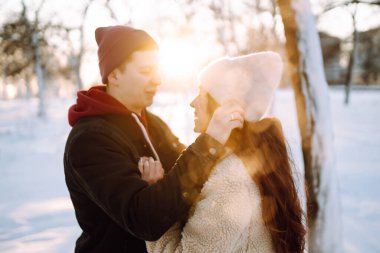 Genç çift kış tatilinde, gün batımında karlı bir ormanda. Kış günü kız arkadaşını kucaklayan yakışıklı bir genç. İnsanlar, mevsim, seyahat, aşk ve eğlence konsepti.