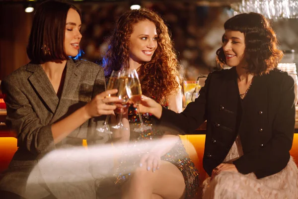 Three young Woman with champagne glasses at night club.  Women friends drinking champagne  in the bar. Party, celebration, friends, bachelorette party, birthday, winter holidays concept.