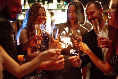 Arkadaşlar yılbaşı partisini maytap ve şampanyayla kutlarlar. Bir grup mutlu insan havai fişeklerle eğleniyor. Kış tatili, gençlik, yaşam tarzı konsepti..